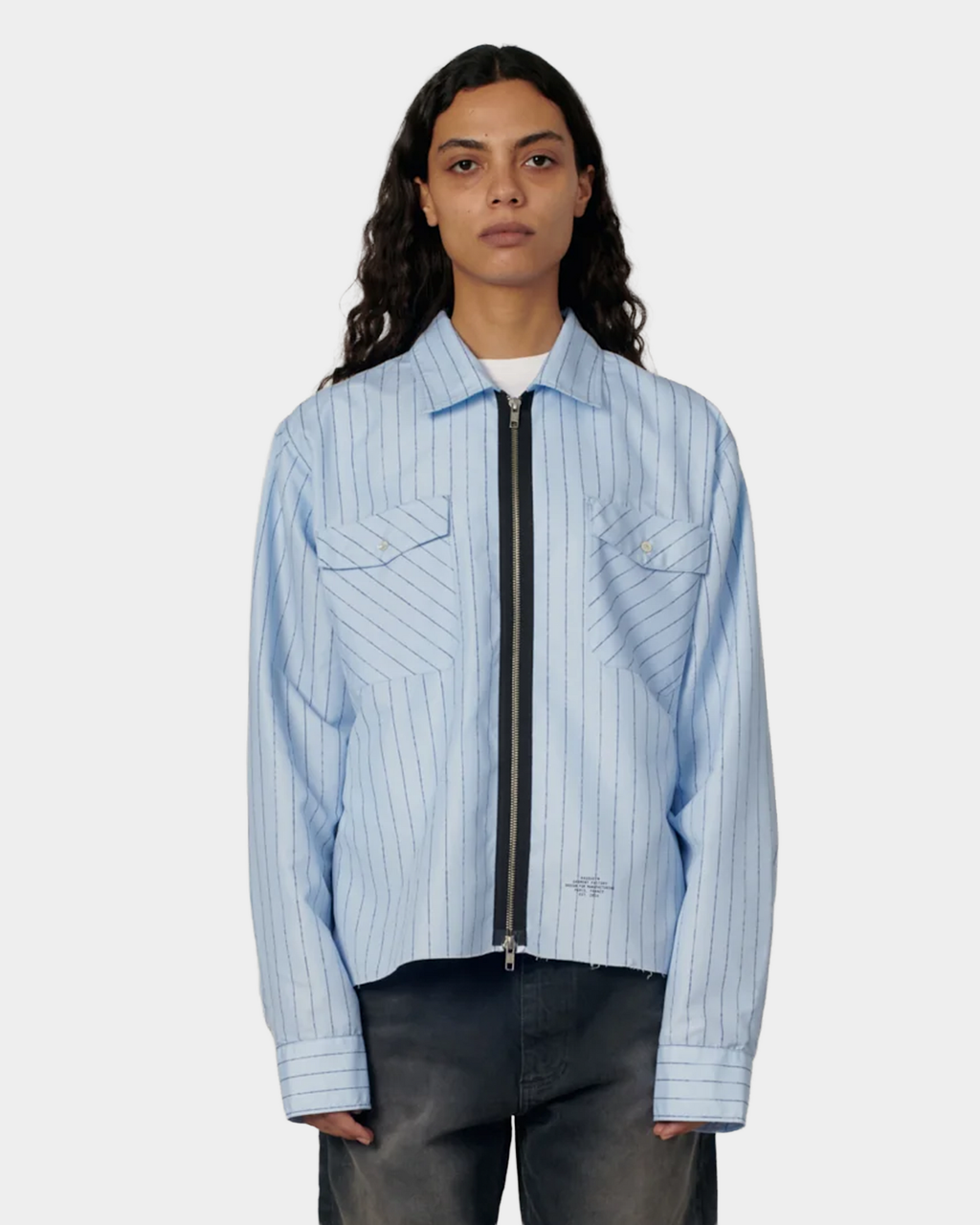 A model wearing the pale blue pinstripe Rassvet Striped Loose Zip Shirt open at the neck over a white tee, with the boxy cropped hem sitting at the waist