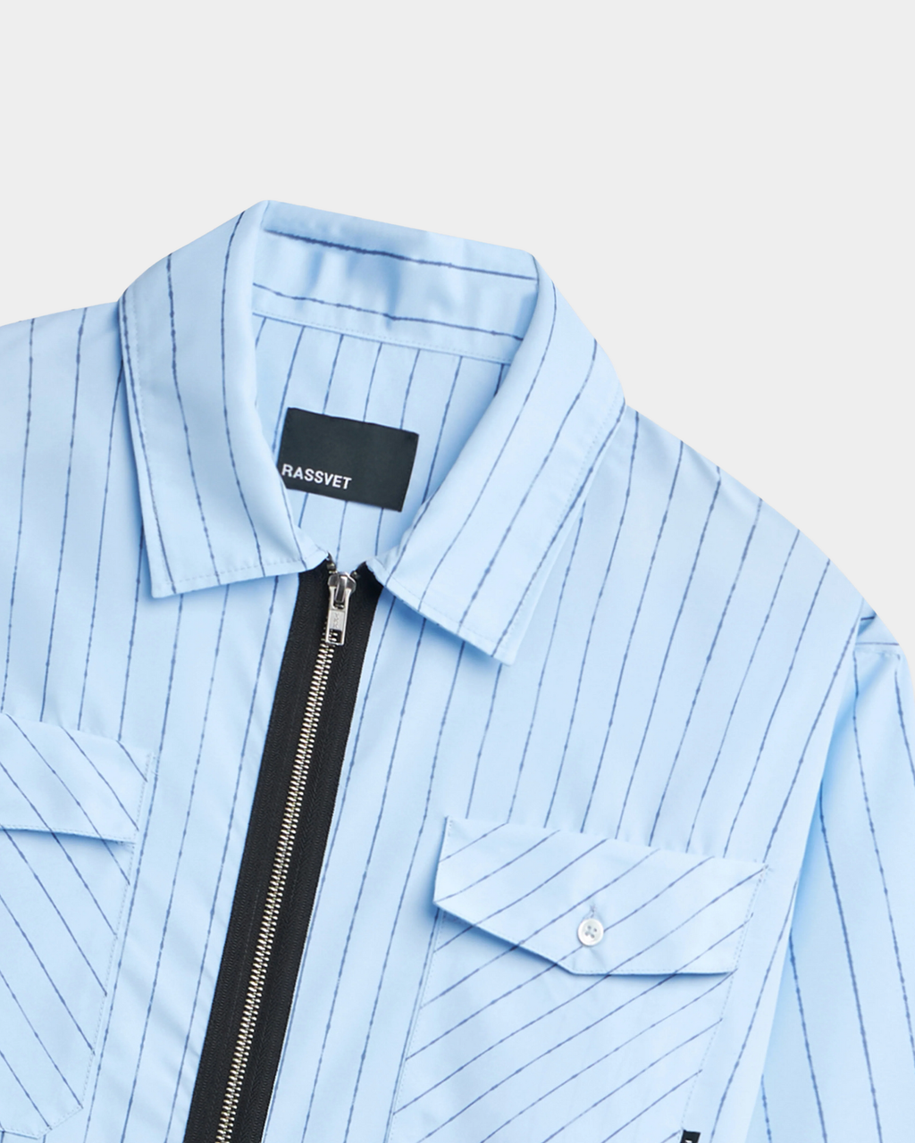 Close-up of the Rassvet Striped Loose Zip Shirt collar and chest, showing the point collar, the exposed black zip tape, a black folded Rassvet label and the pale button on the pocket flap