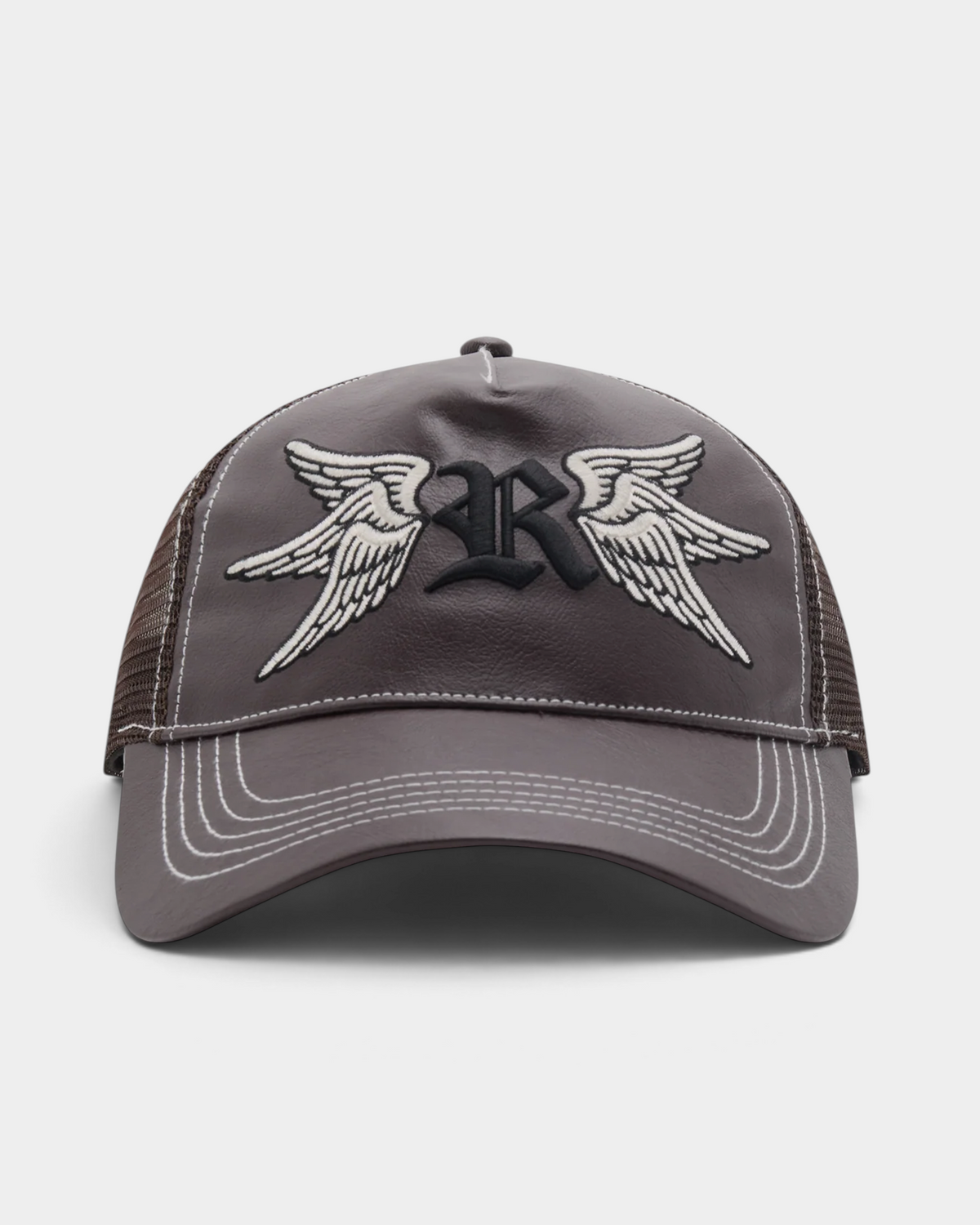 Rassvet Swallows Trucker Cap in brown, shown front on, with a smooth leather-look front panel, dark brown mesh sides, rows of pale contrast stitching on the brim and an embroidered blackletter R flanked by cream wings