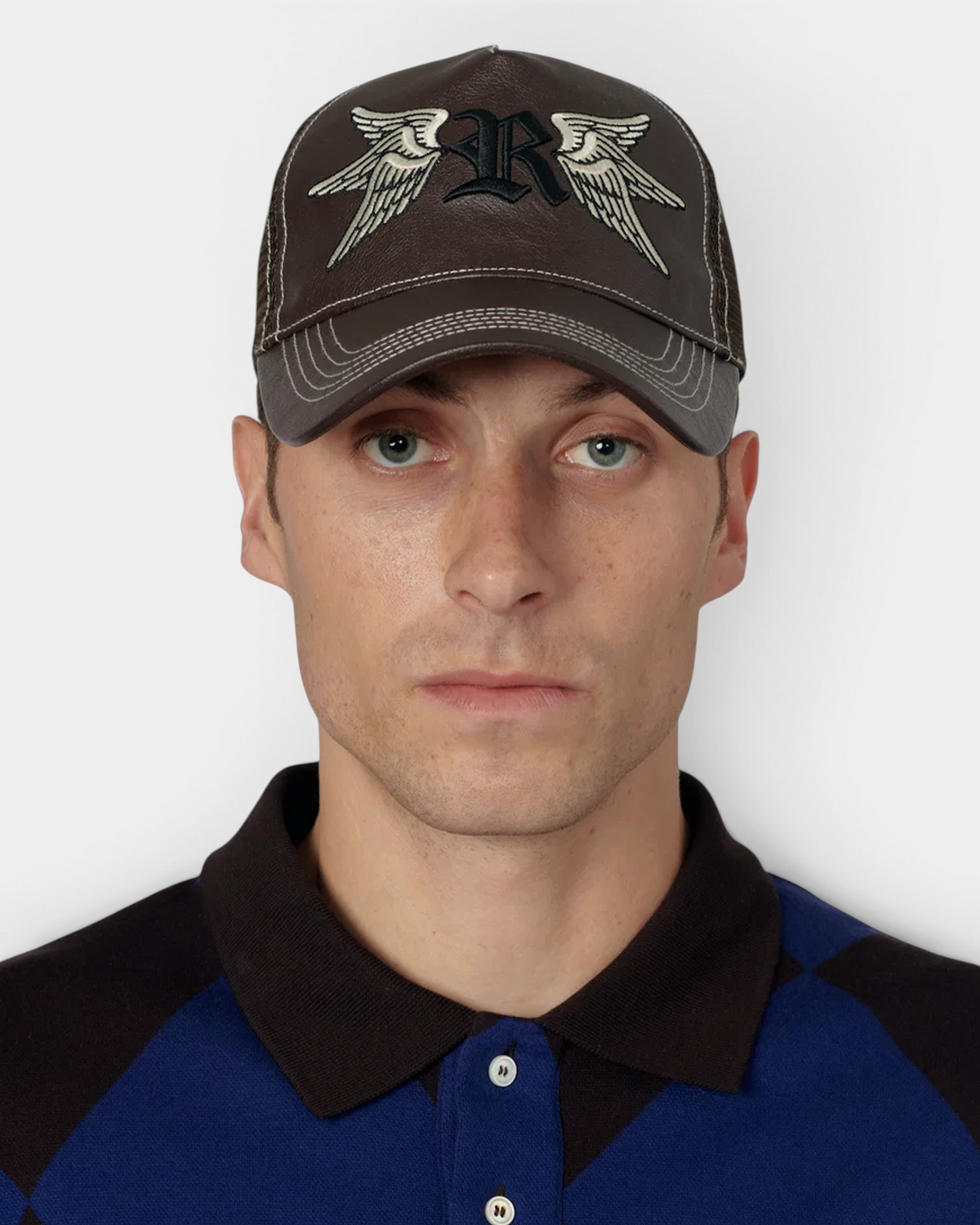 A man wearing the brown Rassvet Swallows Trucker Cap, the winged R embroidery and the contrast-stitched brim seen straight on