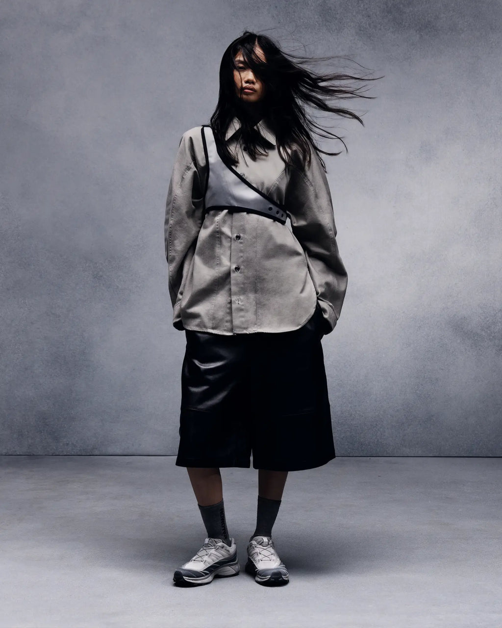 Salomon XT-EVO Shoes in Alloy/Castlerock/Footwear Silver, person standing against a grey studio backdrop in a grey jacket and black shorts, hair blown sideways, wearing the shoes