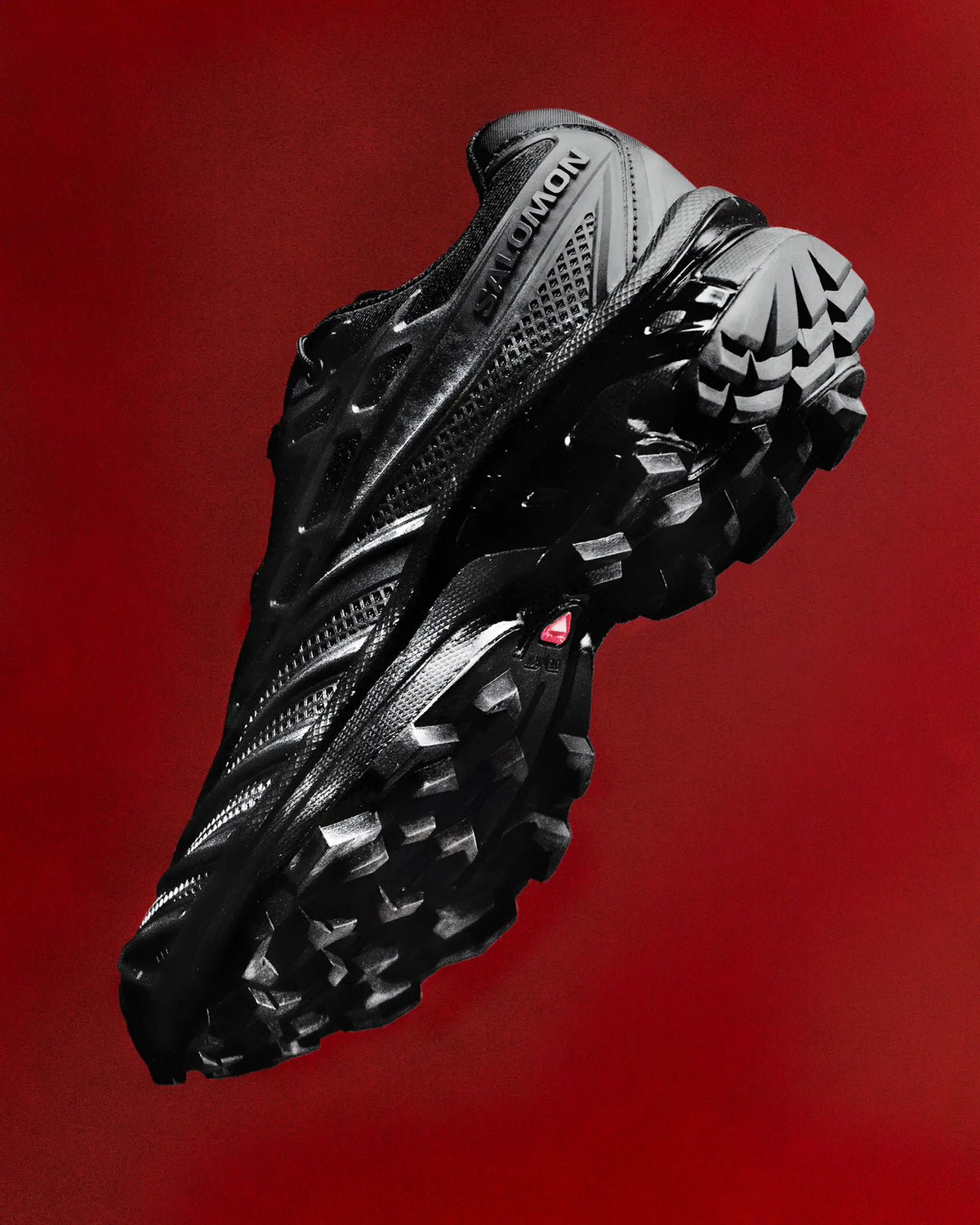 Salomon XT-EVO Shoes in Black/Black/Asphalt, single shoe suspended against a deep red backdrop, outsole tilted toward the camera