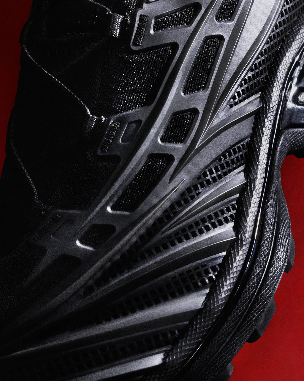 Salomon XT-EVO Shoes in Black/Black/Asphalt, close-up of the upper's mesh and moulded overlays against a red backdrop