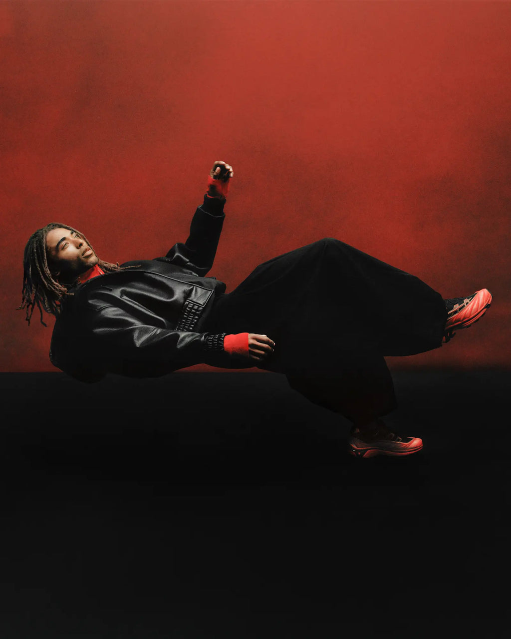 Salomon XT-EVO Shoes in Black/Fiery Red/White, person lying back against a dark red backdrop, dressed in black, wearing the shoes