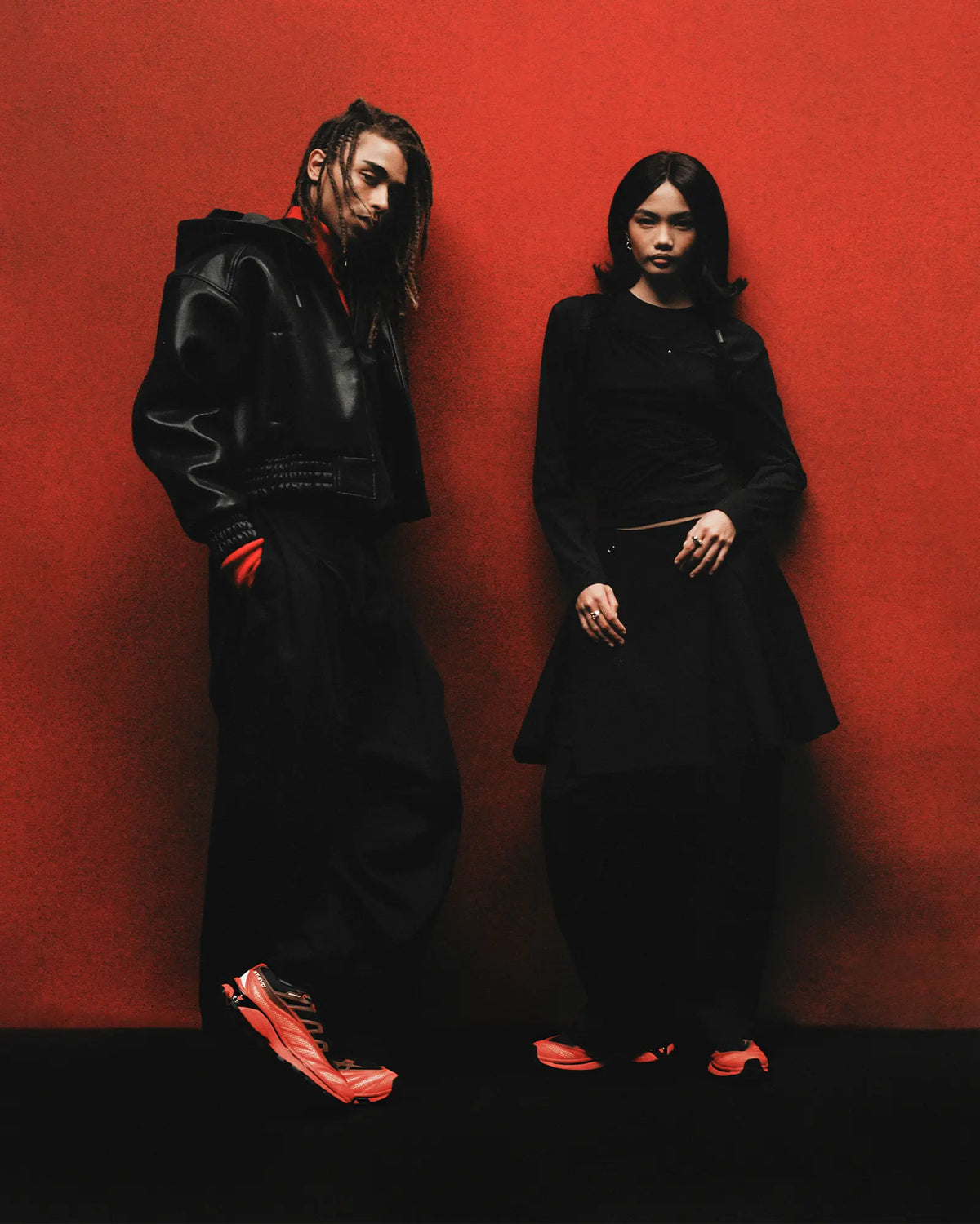 Salomon XT-EVO Shoes in Black/Fiery Red/White, two people standing side by side against a red backdrop, both dressed in black, both wearing the shoes