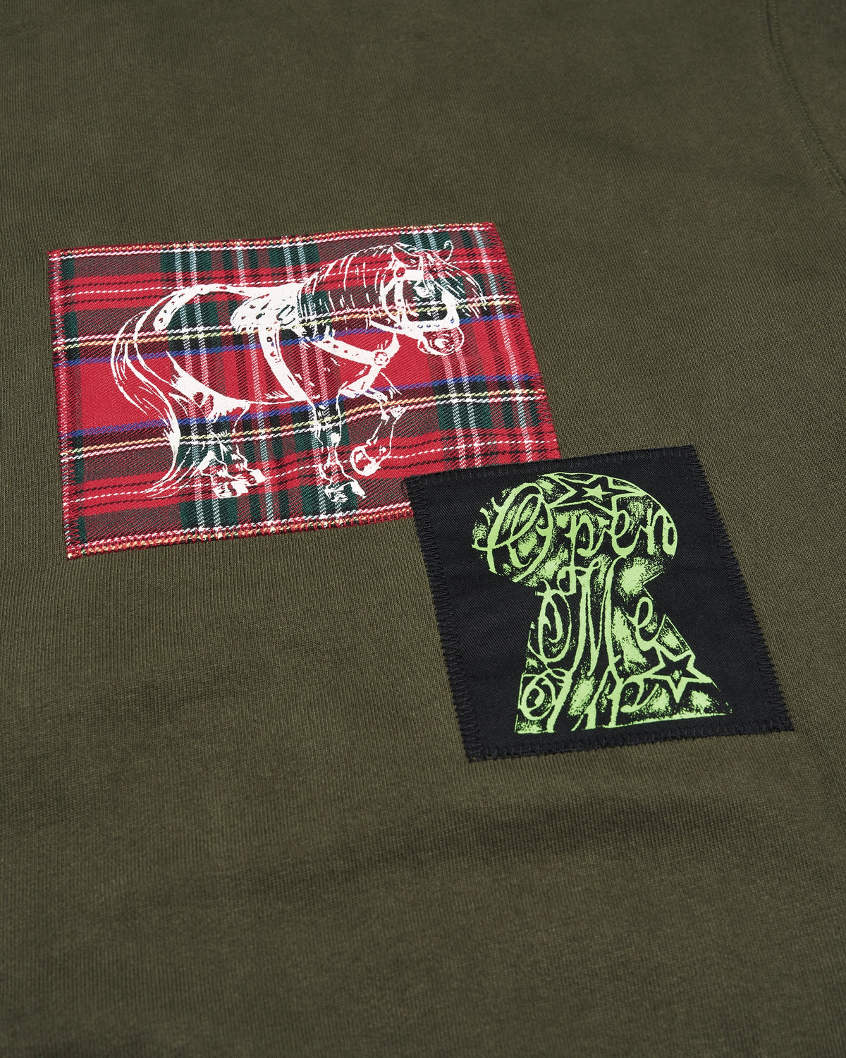 Lockwood Avenue Token Carly zip-up hoodie in olive green with printed and sewn patches, close up of a red tartan patch and a black patch