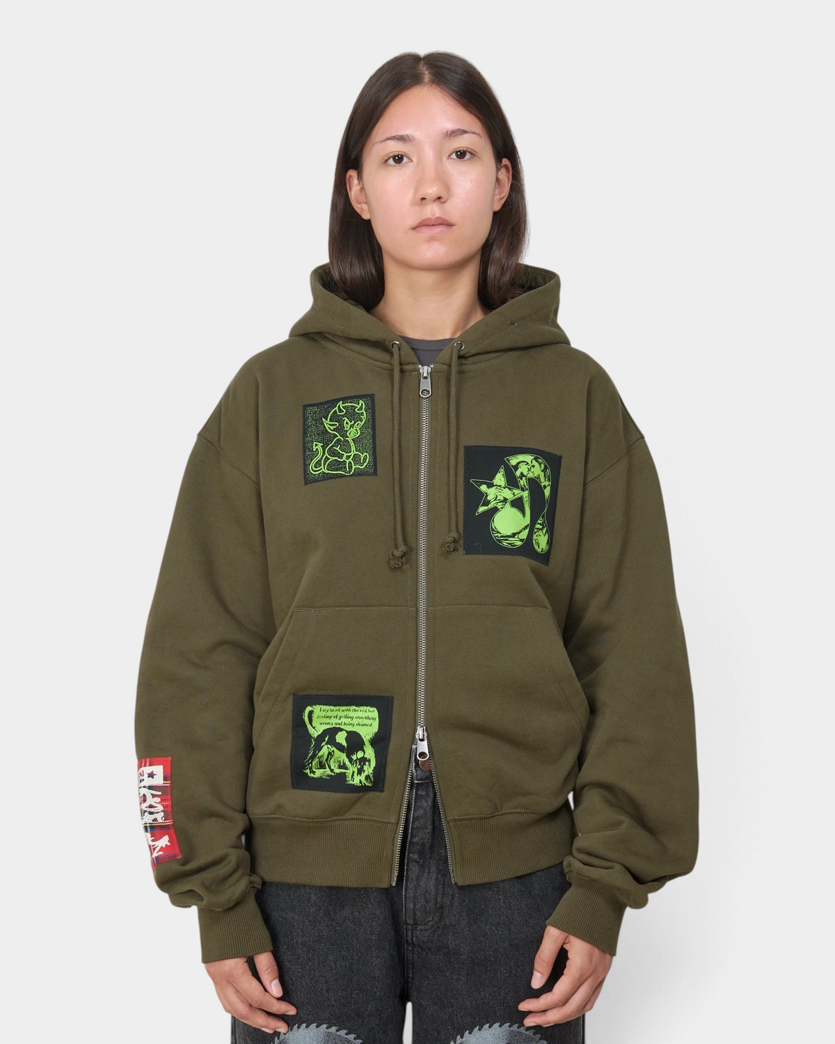 Lockwood Avenue Token Carly zip-up hoodie in olive green with printed and sewn patches, worn by a model, front view