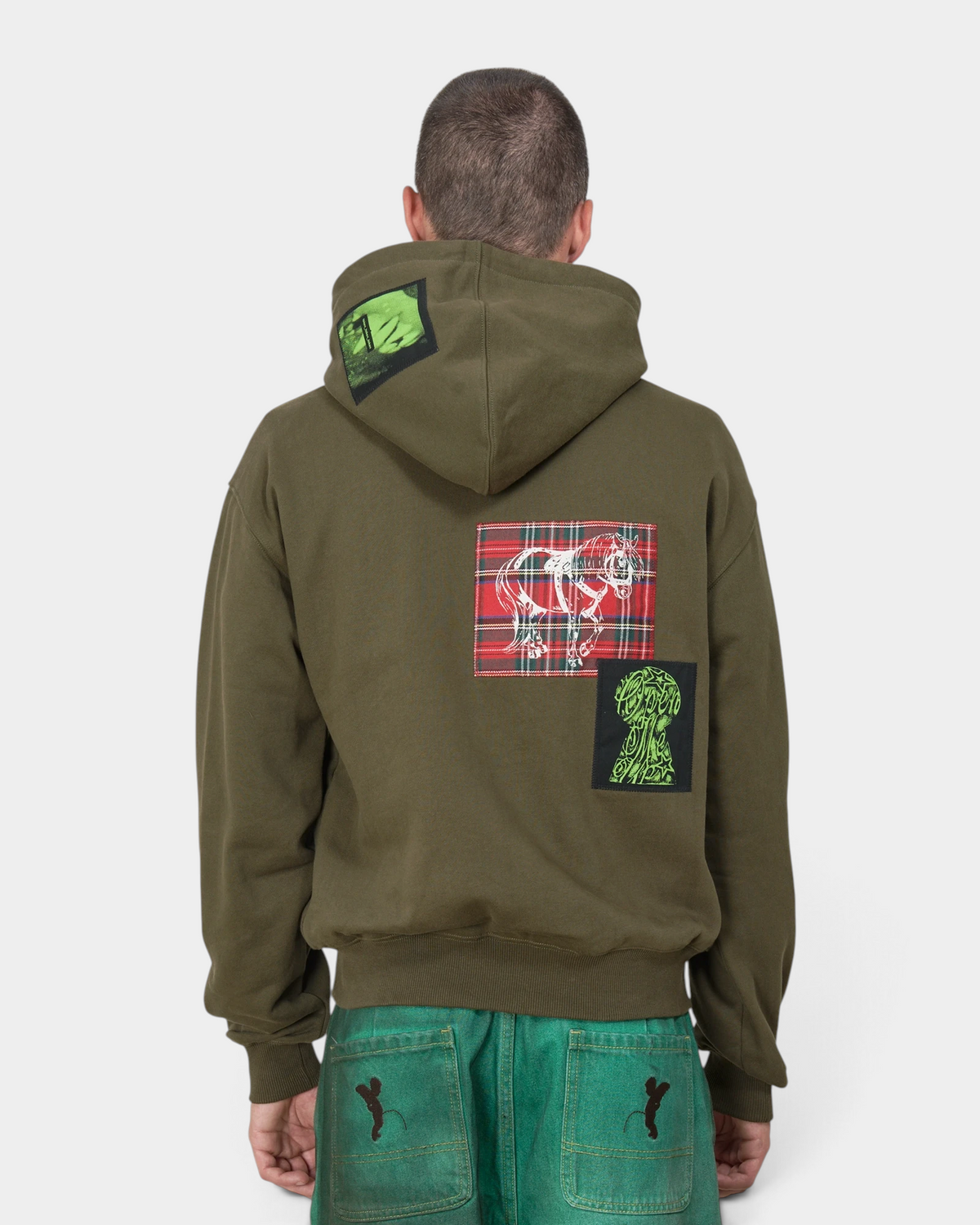 Lockwood Avenue Token Carly zip-up hoodie in olive green with printed and sewn patches, worn by a model, seen from behind