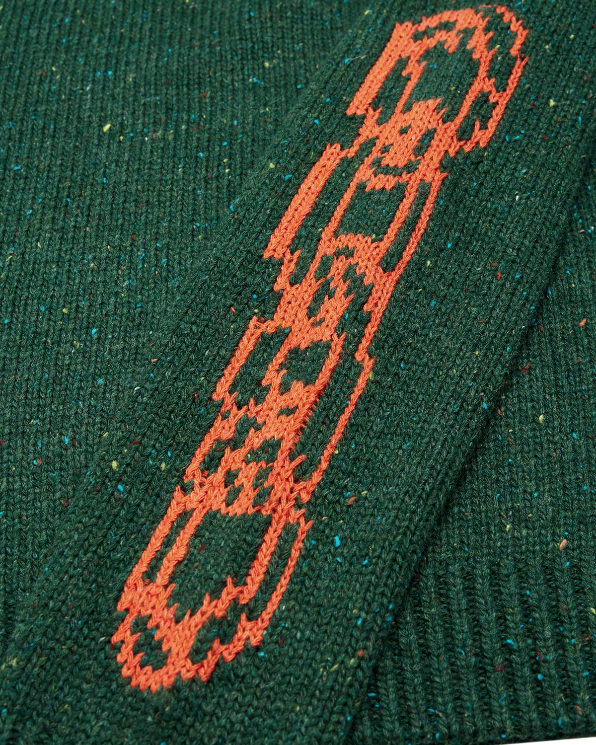 Lockwood Avenue Token Chains sweater, a flecked dark green chunky knit with orange chain jacquard on the sleeves, close up of an orange chain on the sleeve