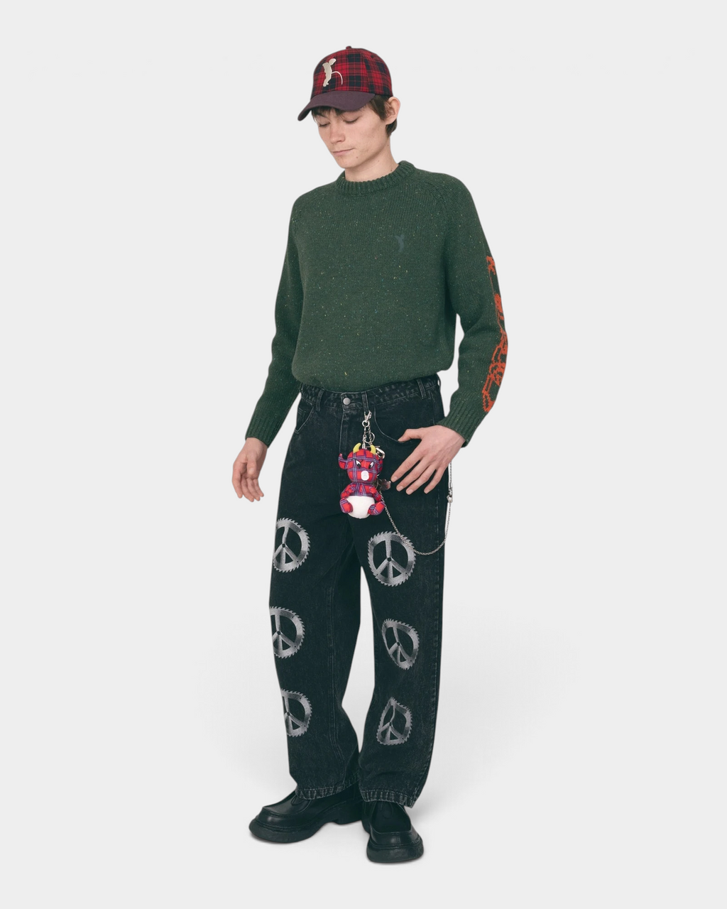 Lockwood Avenue Token Chains sweater, a flecked dark green chunky knit with orange chain jacquard on the sleeves, worn by a model, full length with dark trousers