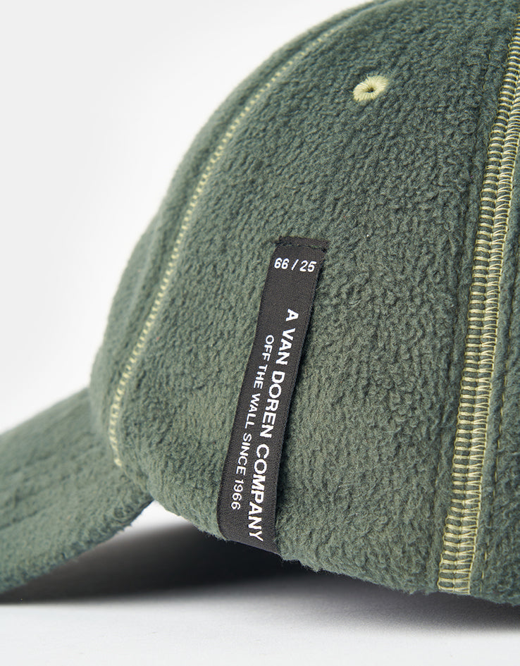 Close up of the black woven side label on the Vans Doren cap, reading 66 / 25, A VAN DOREN COMPANY, OFF THE WALL SINCE 1966, against the green fleece